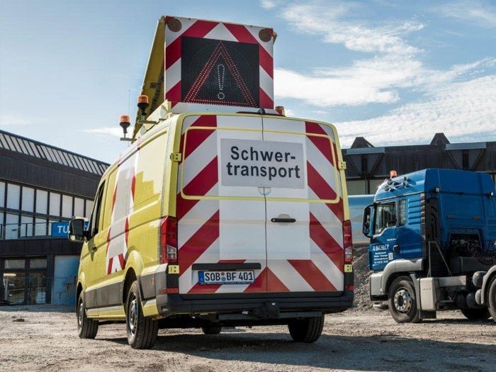 Begleitfahrzeug mit Aufschrift Schwertransport hinter Transport-LKW